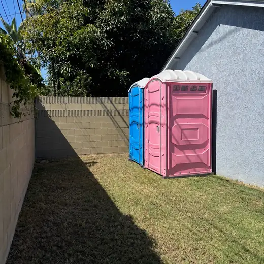 Blue and pink porta potties set on a backyard lawn for a party