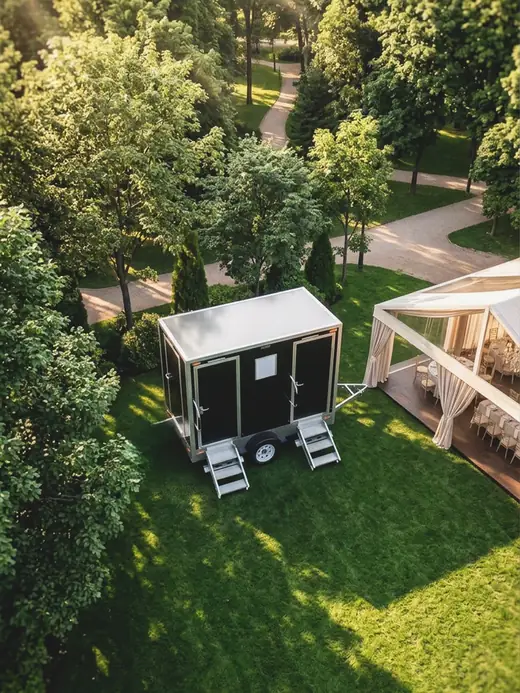 Restroom trailer parked on a lawn beside a garden wedding setup